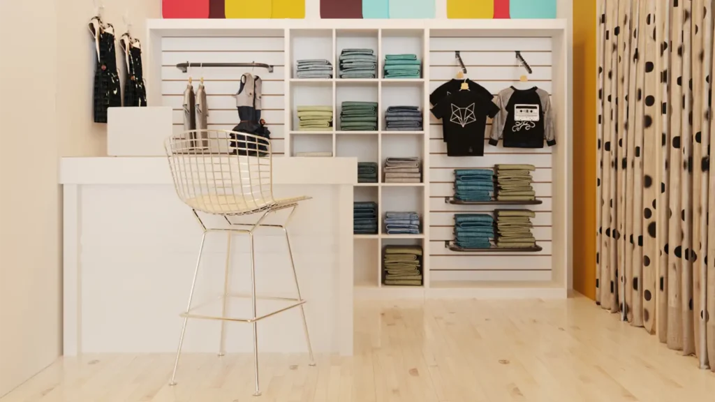 Foto de fundo de loja de roupa infantil. À esquerda é possível ver uma cortina com bolinhas que, provavelmente, leva a um provador, ao fundo está um painel com roupas expostas de diferentes formas e, no canto esquerdo, está o balcão branco de pagamento com um notebook e uma cadeira moderna. A foto é um exemplo de ambiente com decoração para loja infantil.