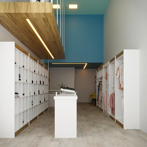  A imagem mostra o interior de uma loja de roupas pequena e simples com um esquema de cores neutras. Ao centro, há um balcão branco que pode ser utilizado para atendimento ao cliente ou caixa. Acima do balcão, uma estrutura de madeira com iluminação embutida adiciona um toque moderno ao espaço. Nas paredes laterais, armários brancos com nichos expõem diversos itens, possivelmente acessórios como bolsas ou sapatos. À direita, araras de madeira claras estão organizadas com roupas penduradas, exibindo peças de vestuário variadas. O piso é de madeira clara, e a parede do fundo é pintada de azul, criando um contraste agradável com o tom mais sóbrio do resto da decoração.