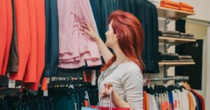 mulher de cabelos ruivos escolhendo roupas penduradas em uma arara de parede